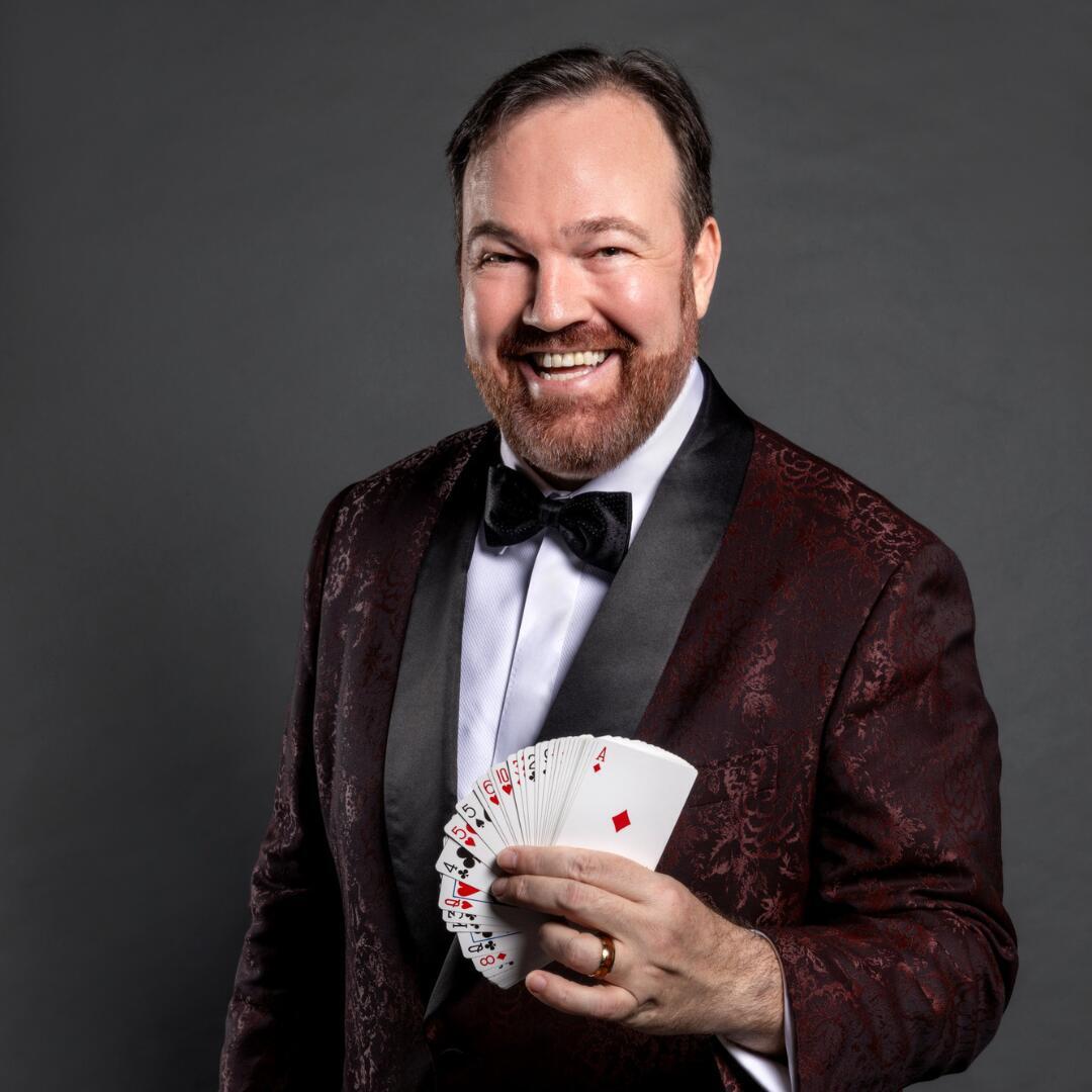 Holding a deck of cards and a promotional flyer, Matt Donnelly exudes confidence, setting the stage for an evening of mesmerizing entertainment.
